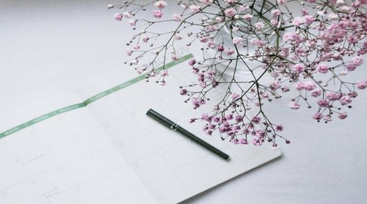 pen laying on an open journal to reflect on year. small flowers top right